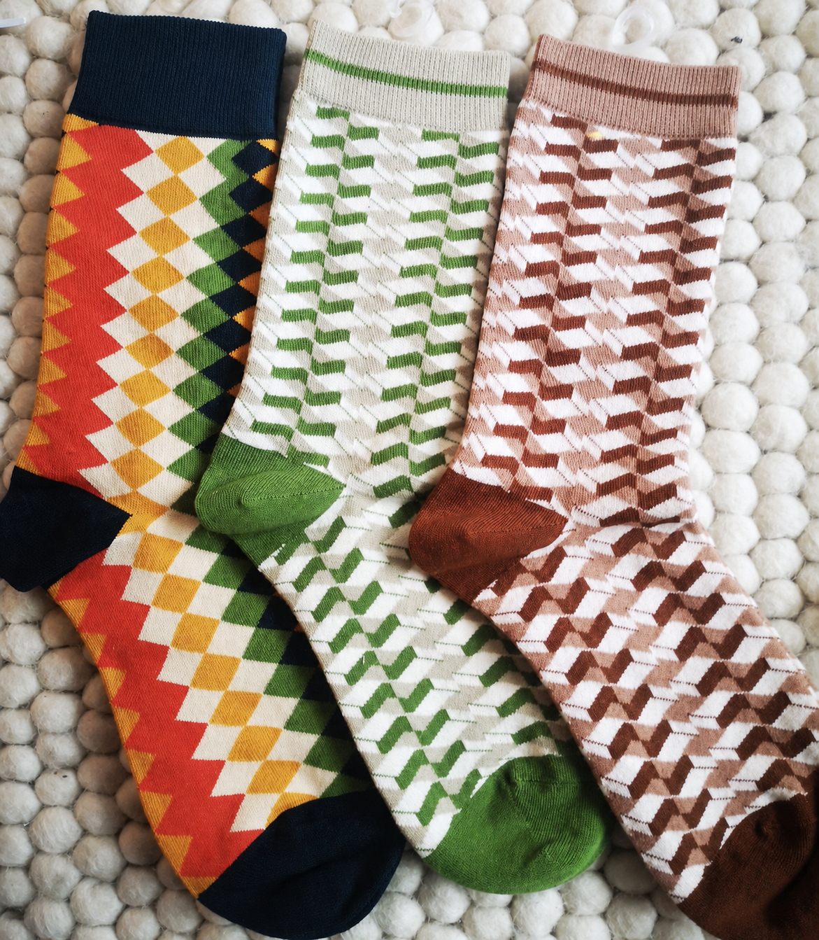 Three colourful Nollaknit socks arranged without labels on a wool rug